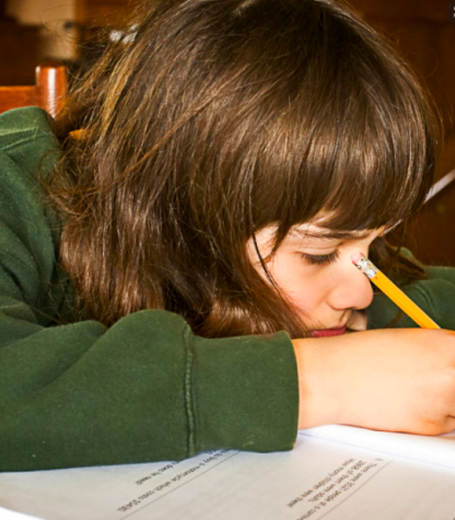 Young girl with head lowered on desk writing on paper